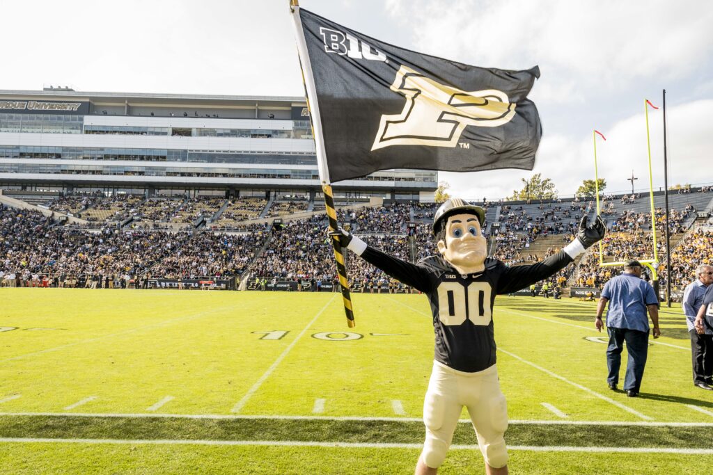 Purdue Pete holding a Purdue flag at a football game