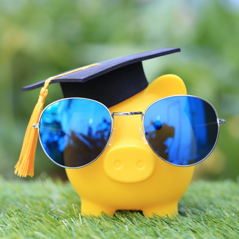 Yellow rubber pig sitting on grass wearing a graduation cap and sunglasses