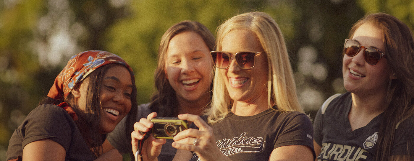 Four women looking at a picture on a camera wearing Purdue gear